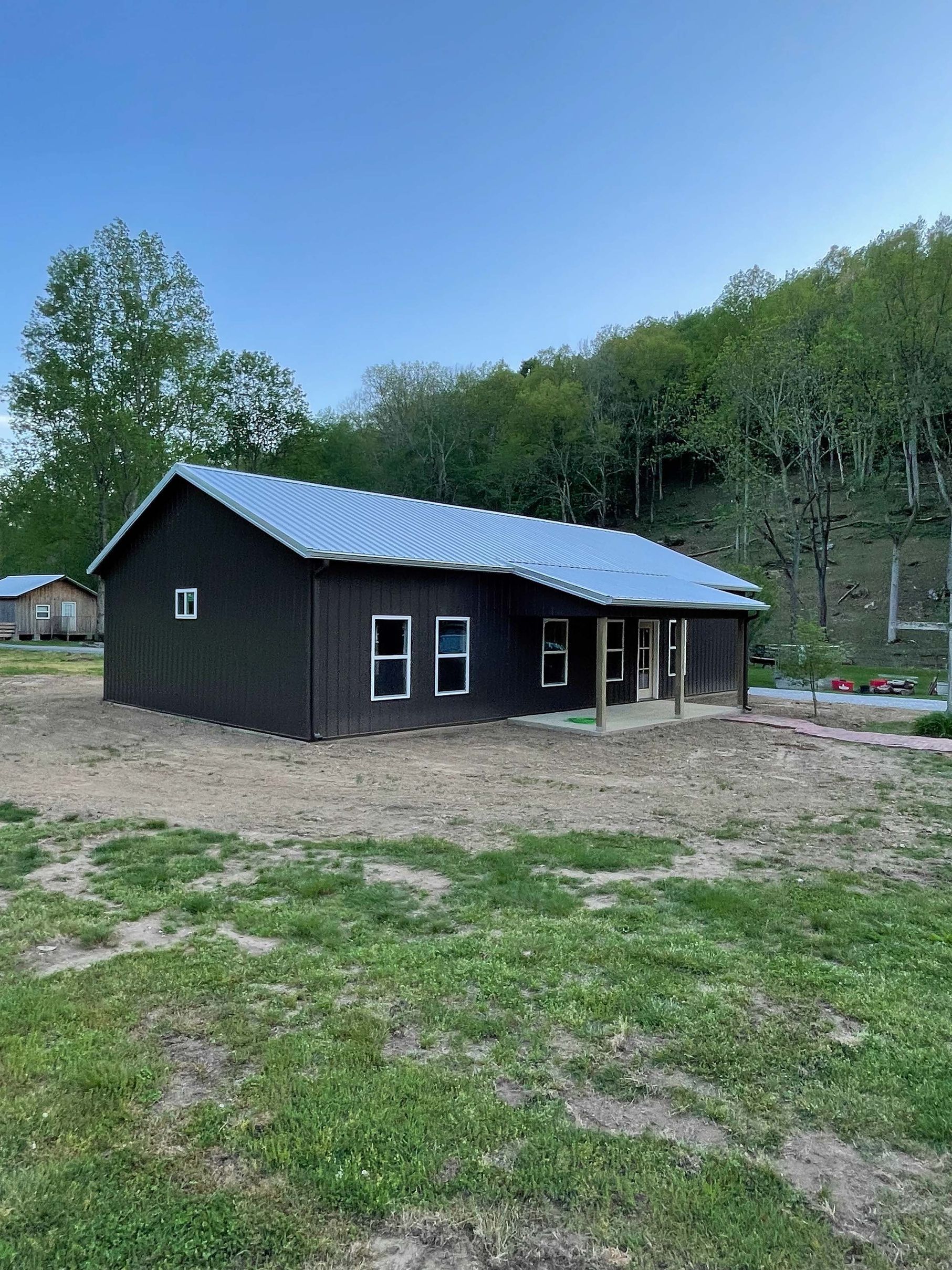 A small black house with a blue roof is sitting in the middle of a grassy field.