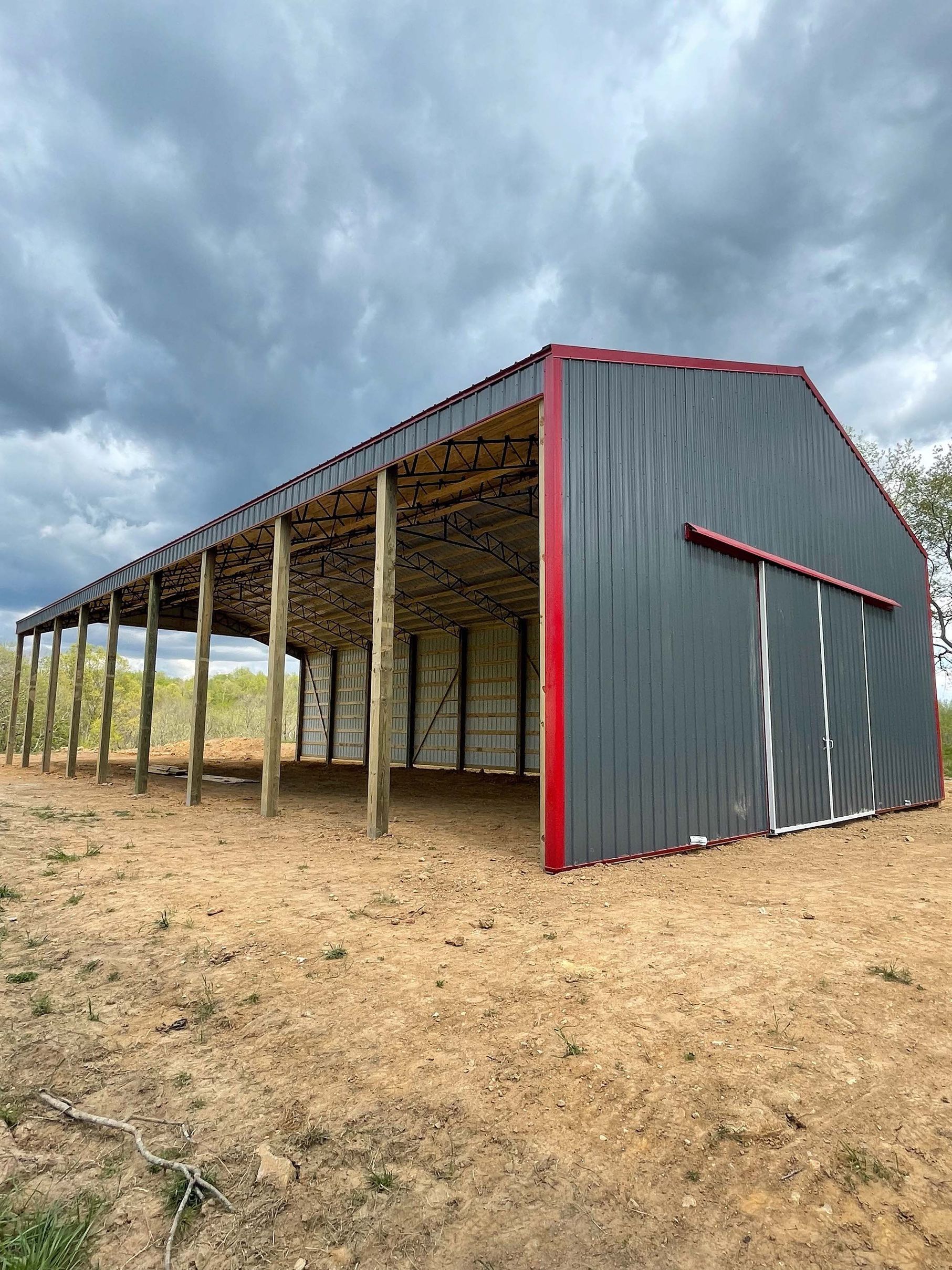 A large barn with a red trim is sitting in the middle of a dirt field.