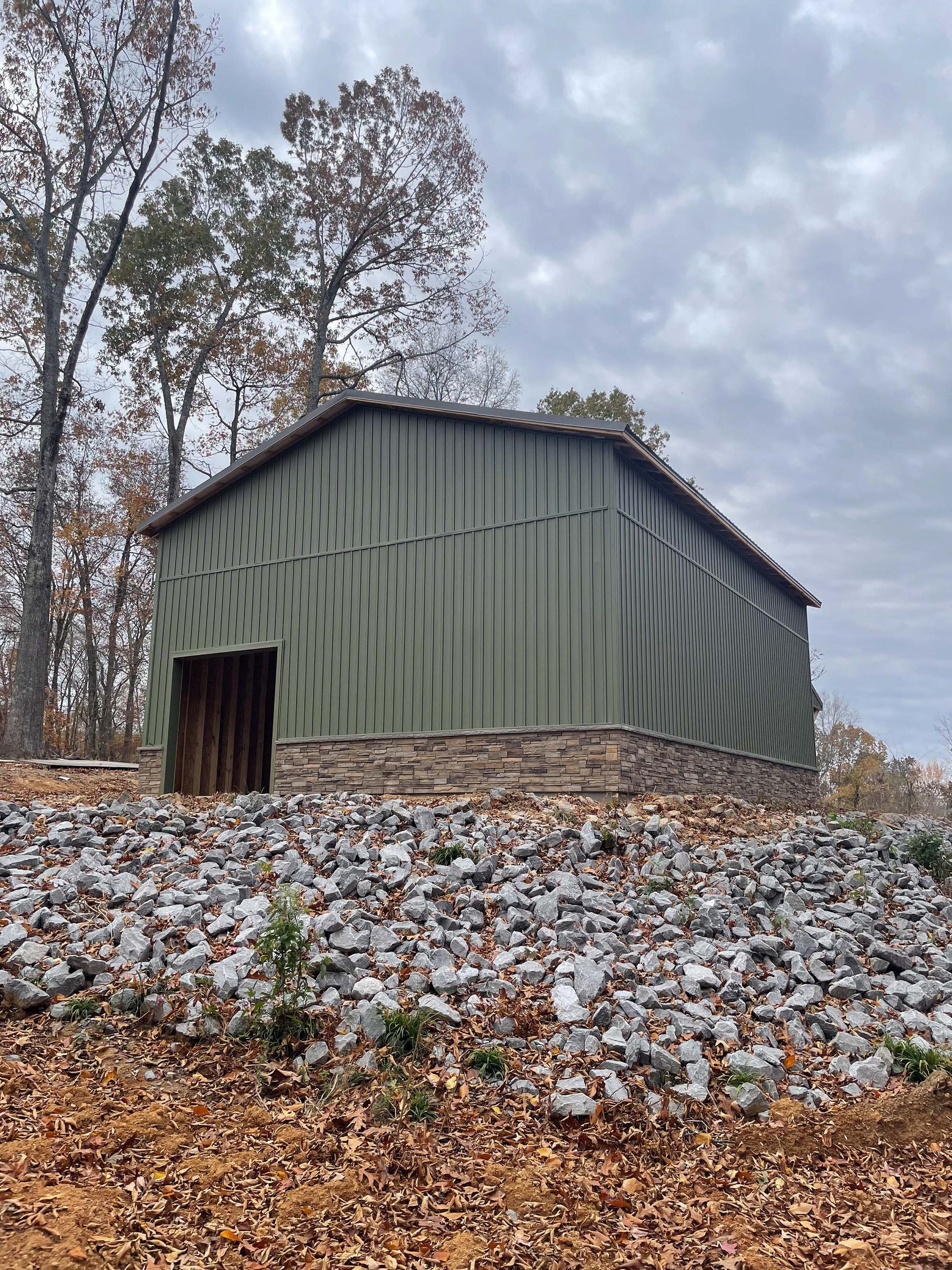 A green barn is sitting on top of a pile of rocks.
