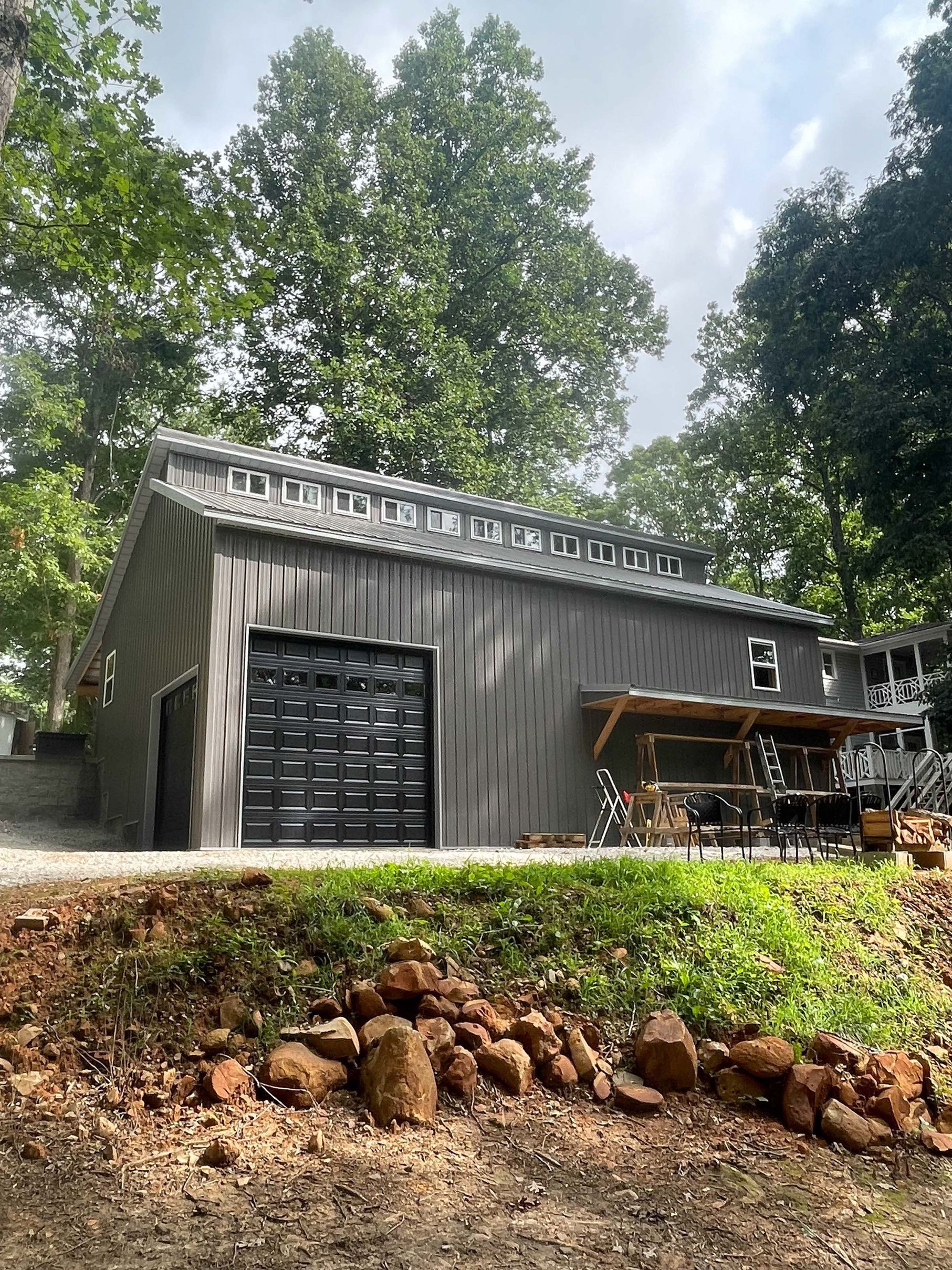 A large gray garage with a black garage door is sitting on top of a grassy hill.