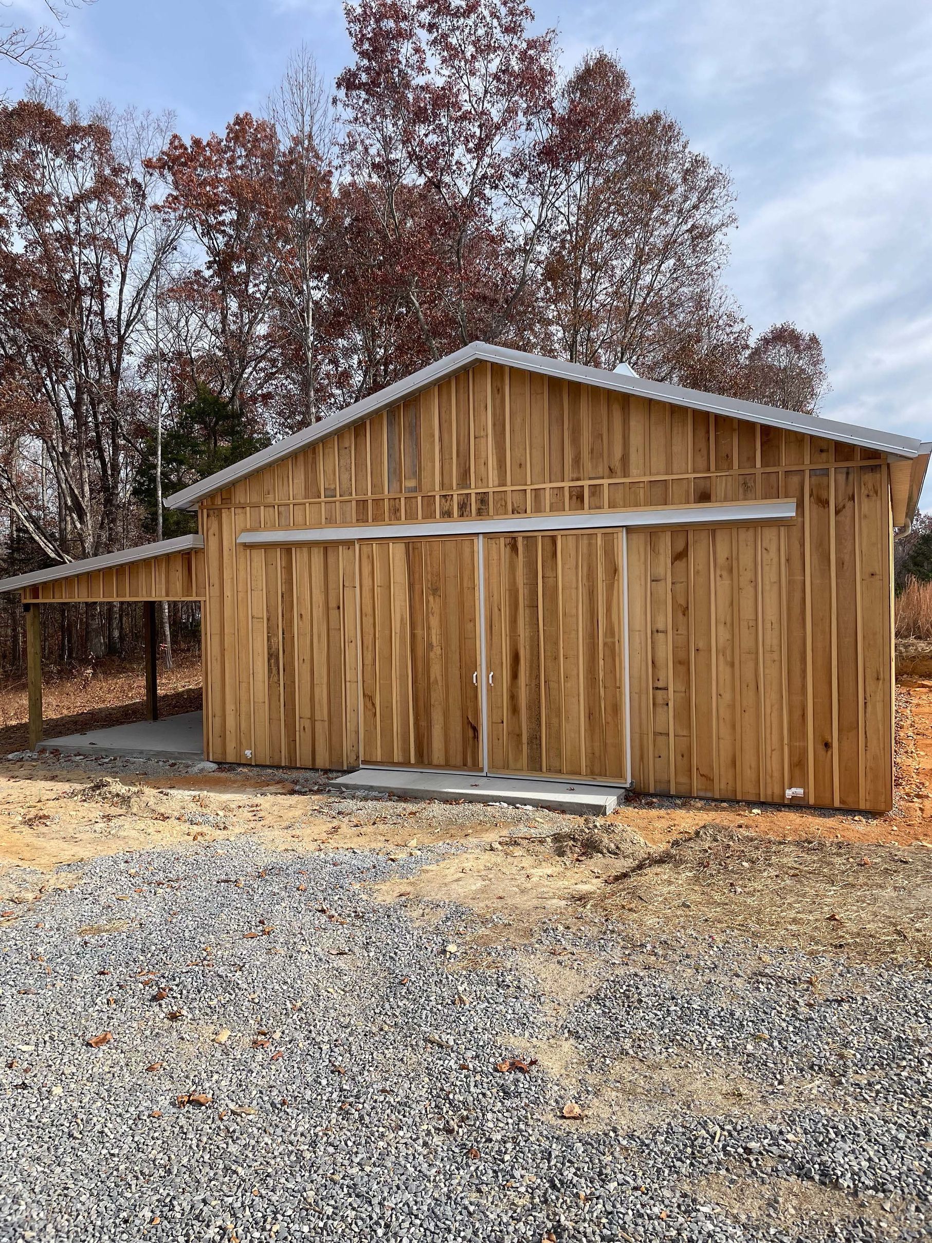 A wooden barn with sliding doors is sitting on top of a gravel lot.
