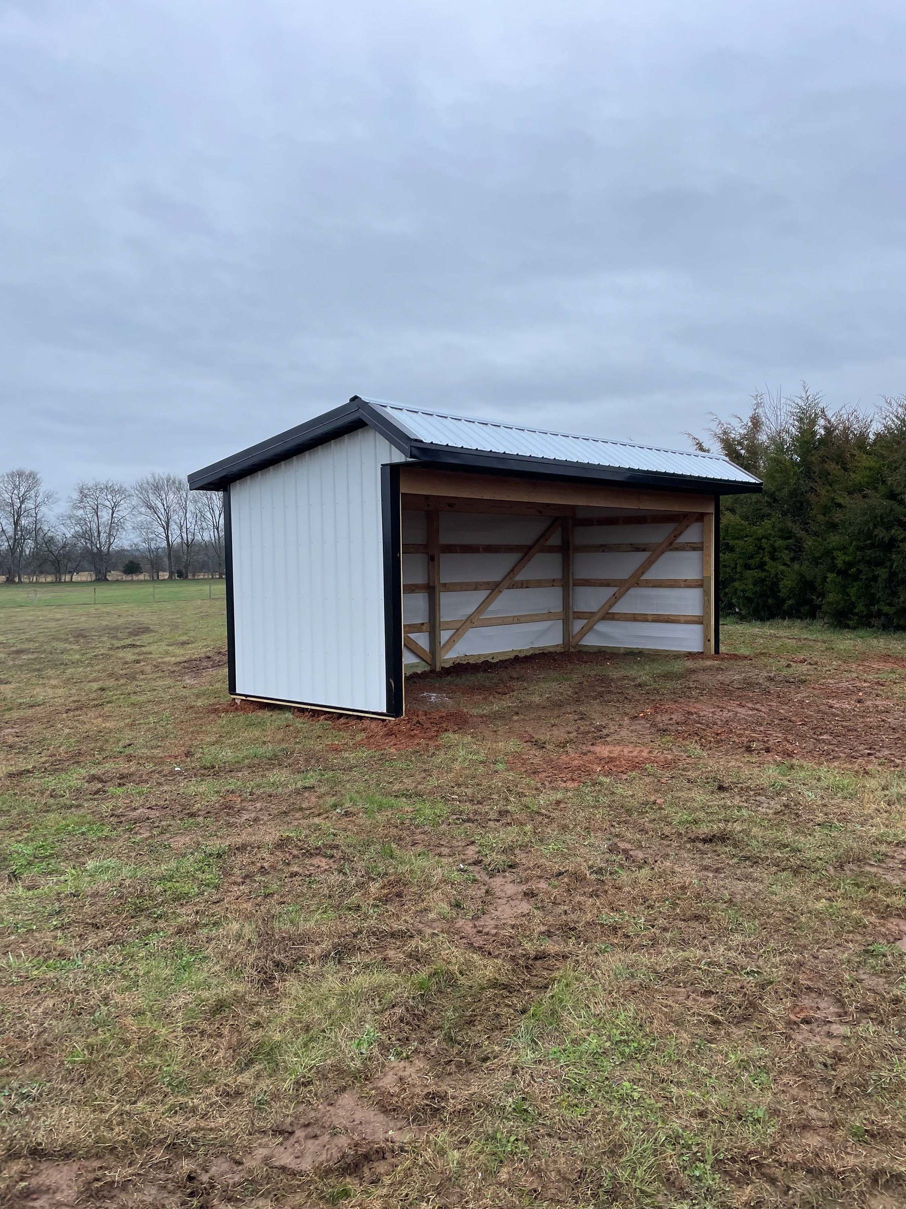 A small white shed is sitting in the middle of a field.