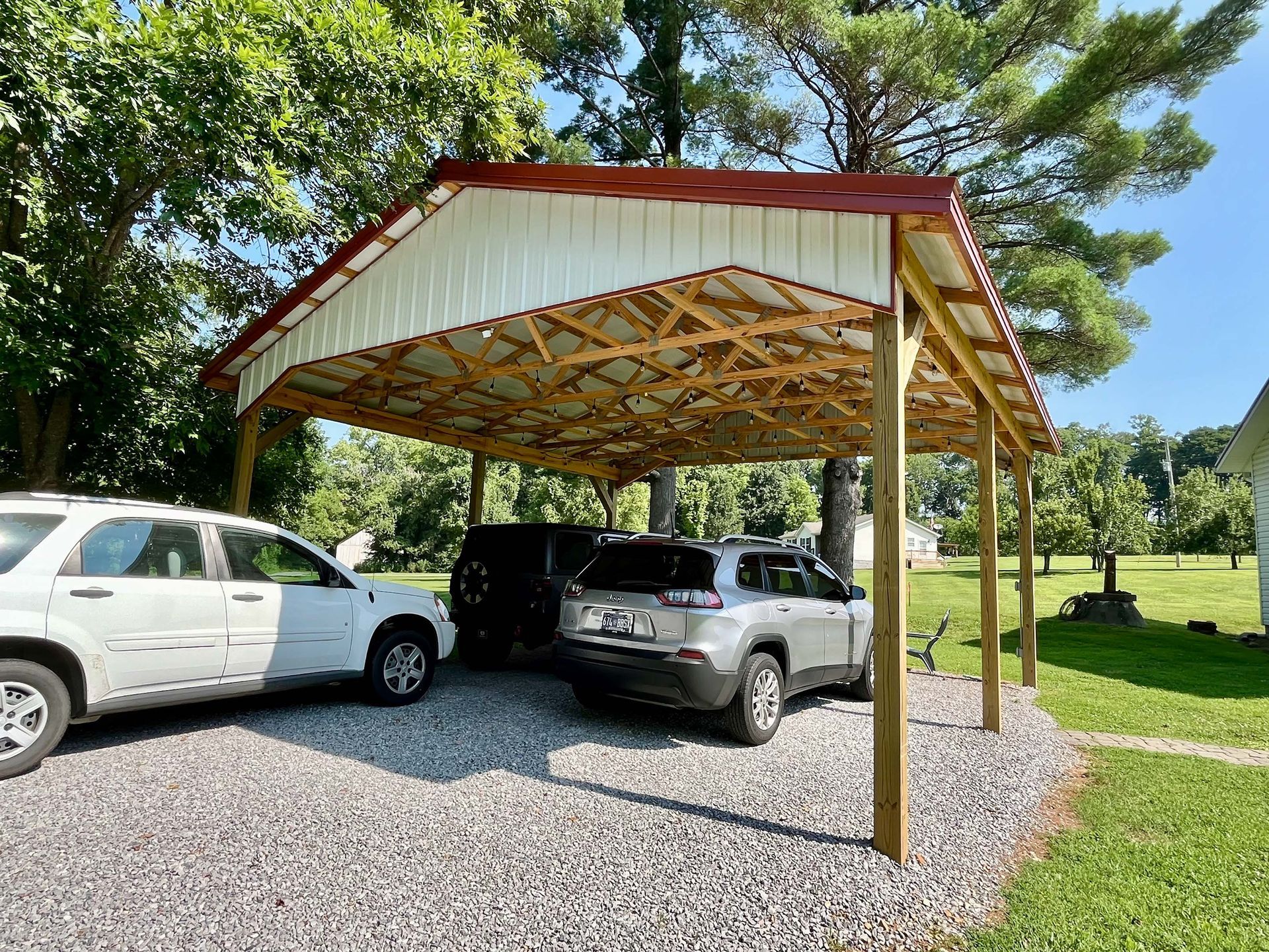 Two cars are parked under a carport in a driveway.