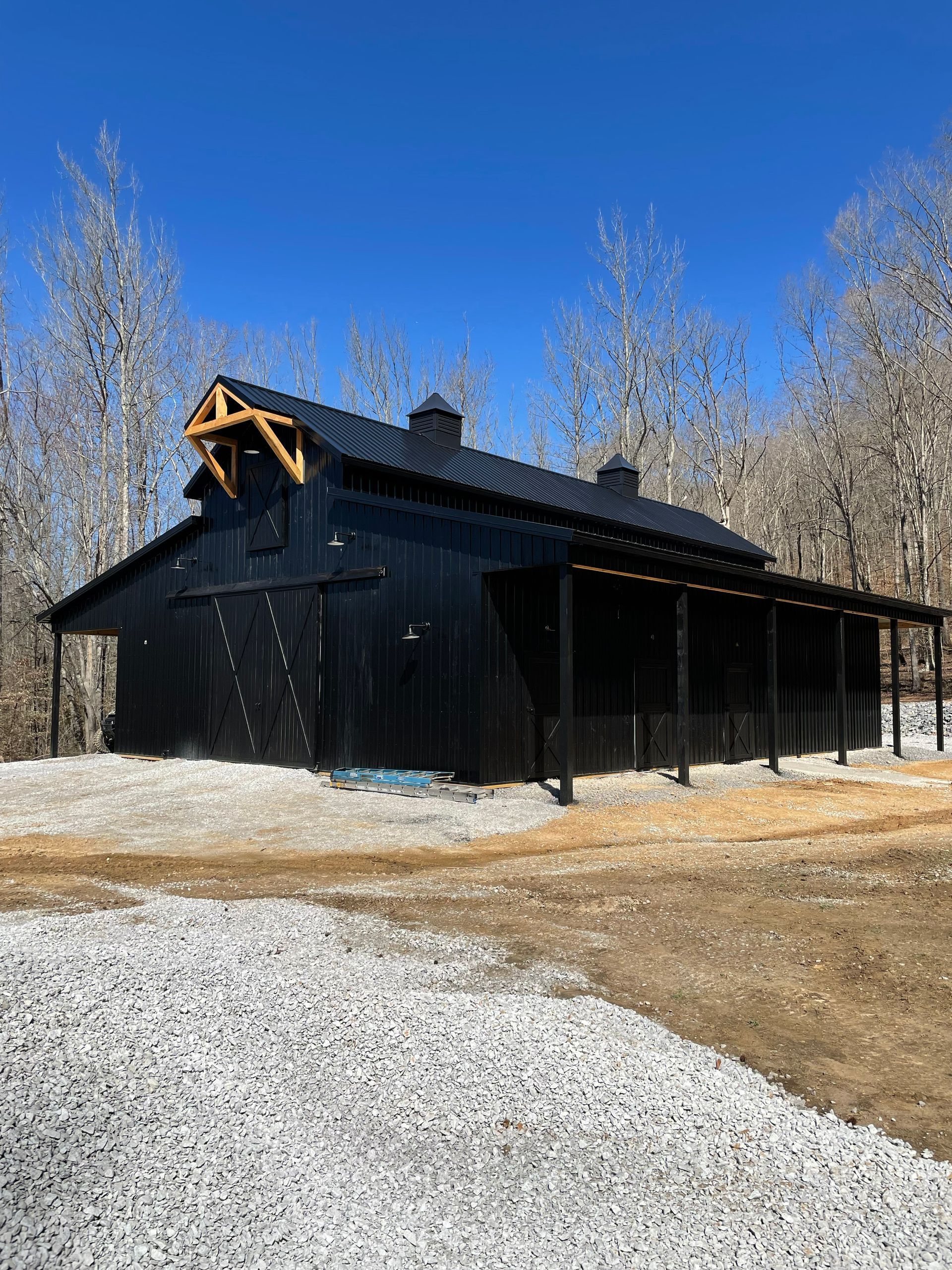 A large black barn is sitting in the middle of a gravel road.