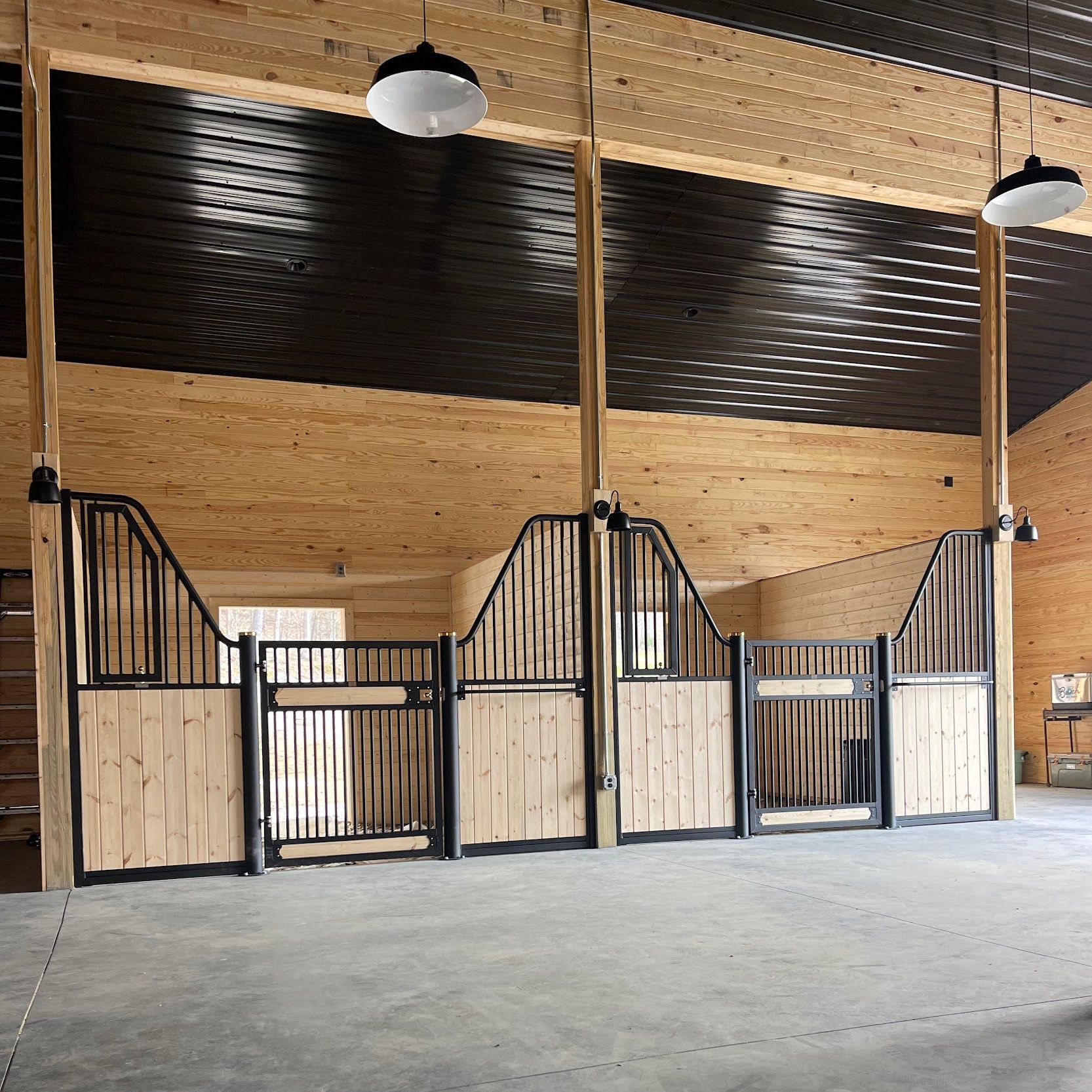 A large empty barn with wooden stalls and a black ceiling.