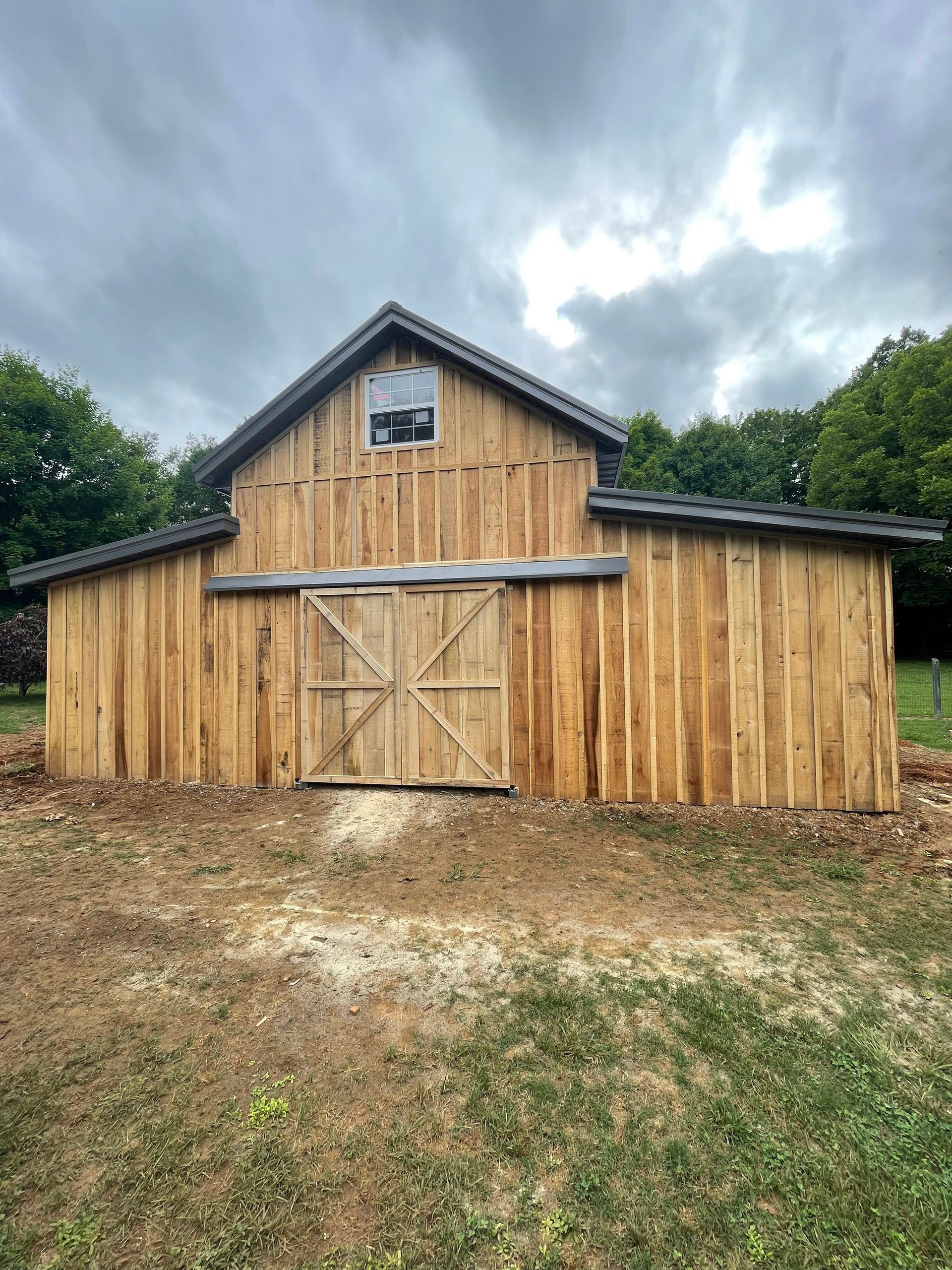 A wooden barn is sitting in the middle of a field.