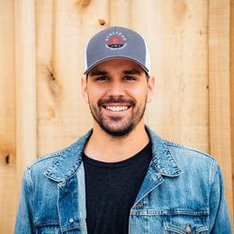 A man wearing a hat and a denim jacket is smiling