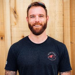 A man with a beard is wearing a black t-shirt with a logo on it