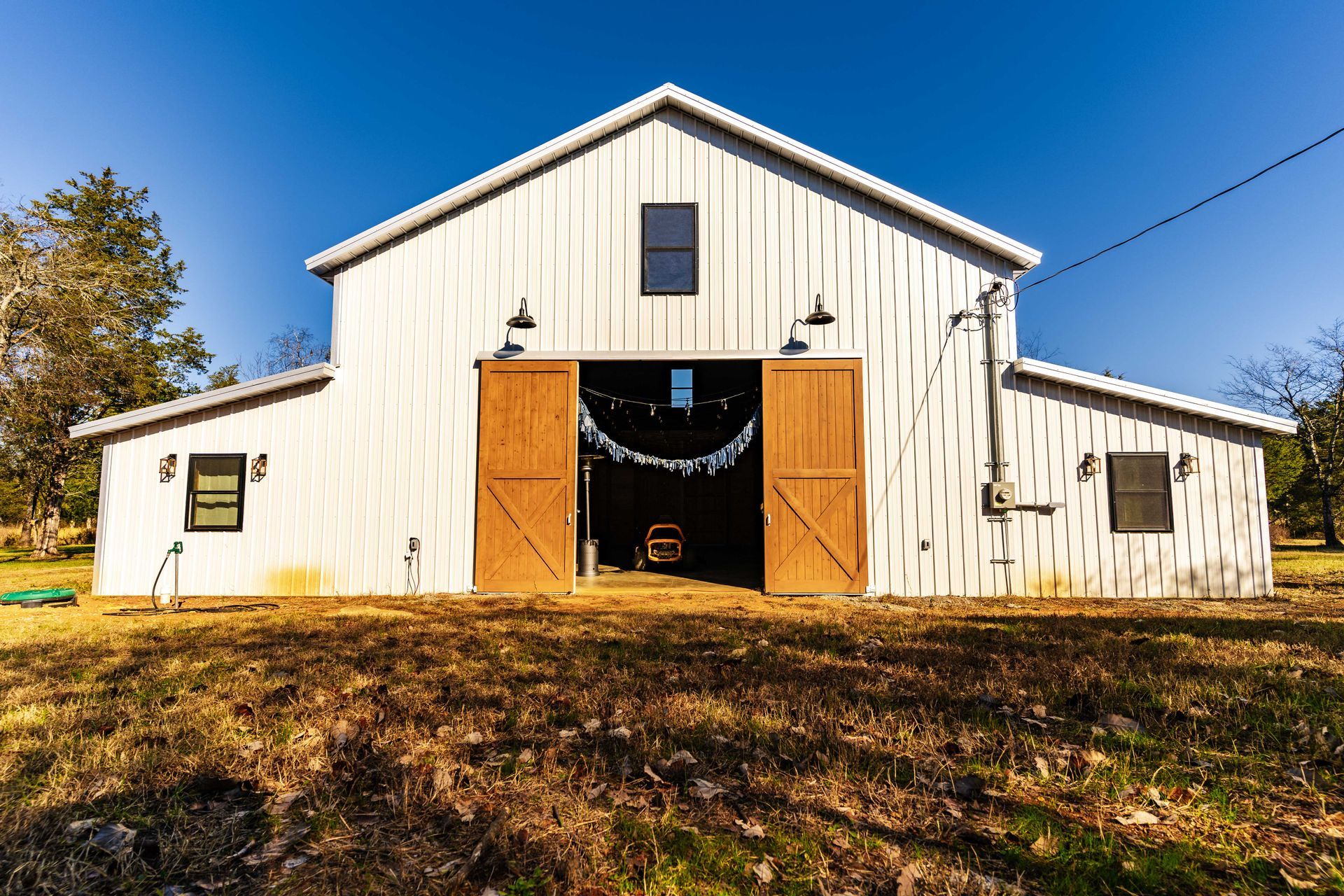 A white barn with wooden doors is sitting in the middle of a field.