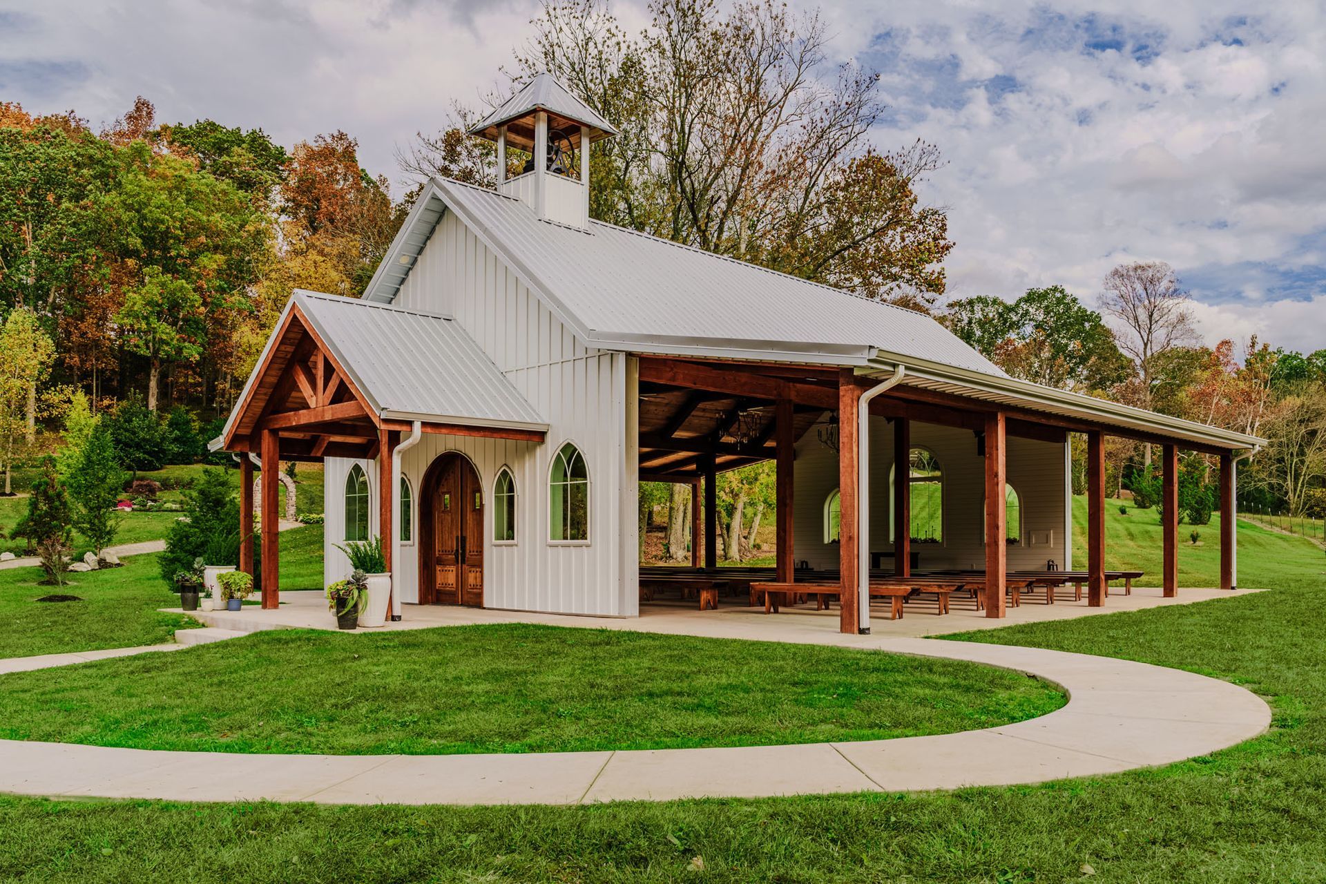 A small white building with a wooden roof is sitting in the middle of a grassy field.