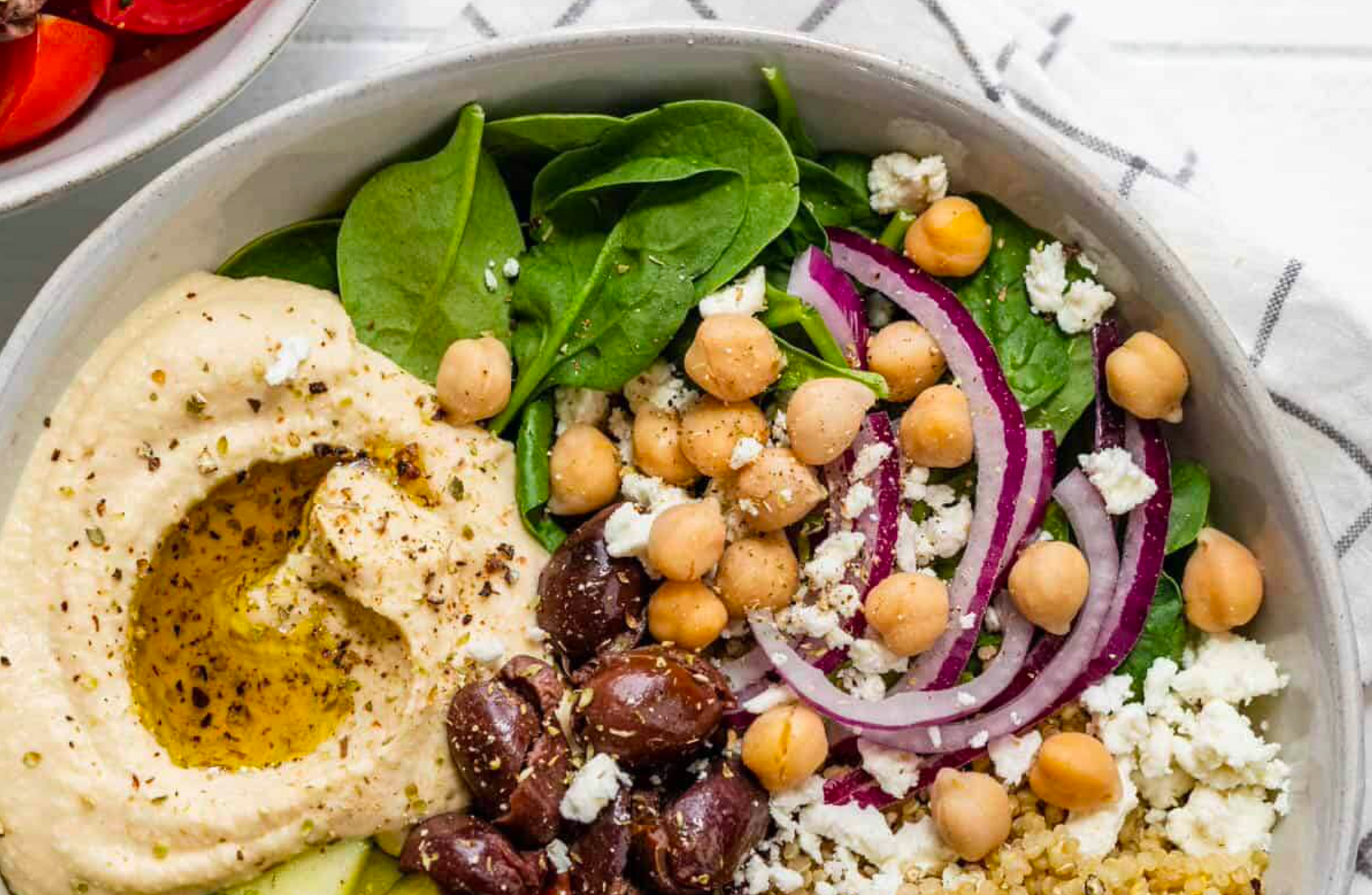 a bowl of food with hummus , chickpeas , olives , spinach and feta cheese .