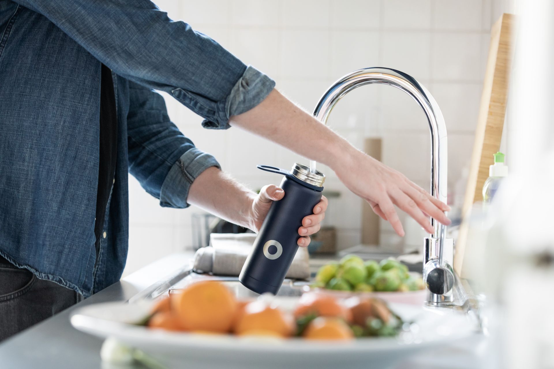 a woman is washing fruit in a kitchen sink while holding a water bottle .