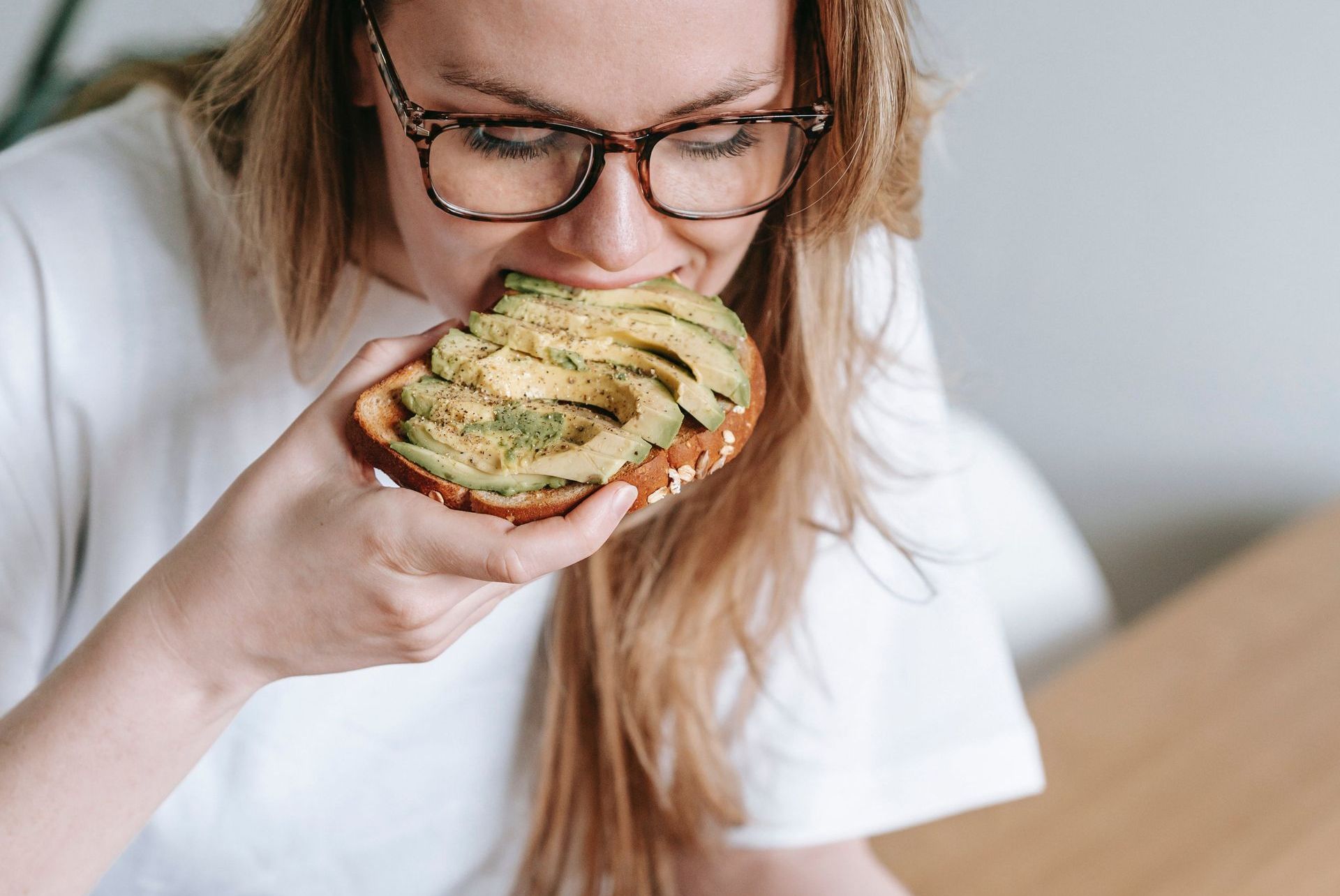 a woman is sitting at a table eating an avocado toast and reading a book .