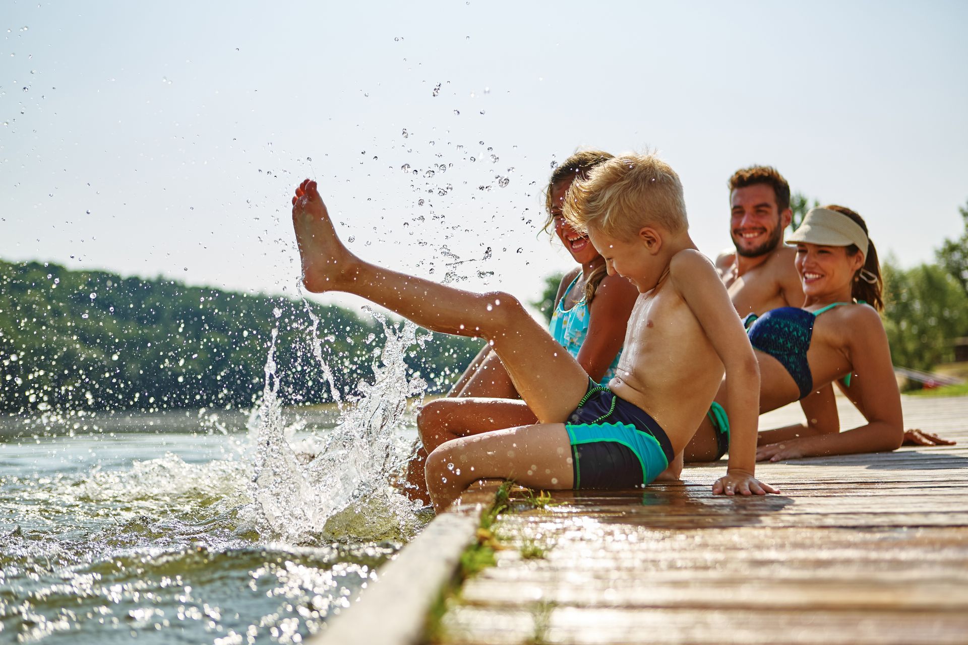 A family is sitting on a dock near a lake splashing water.