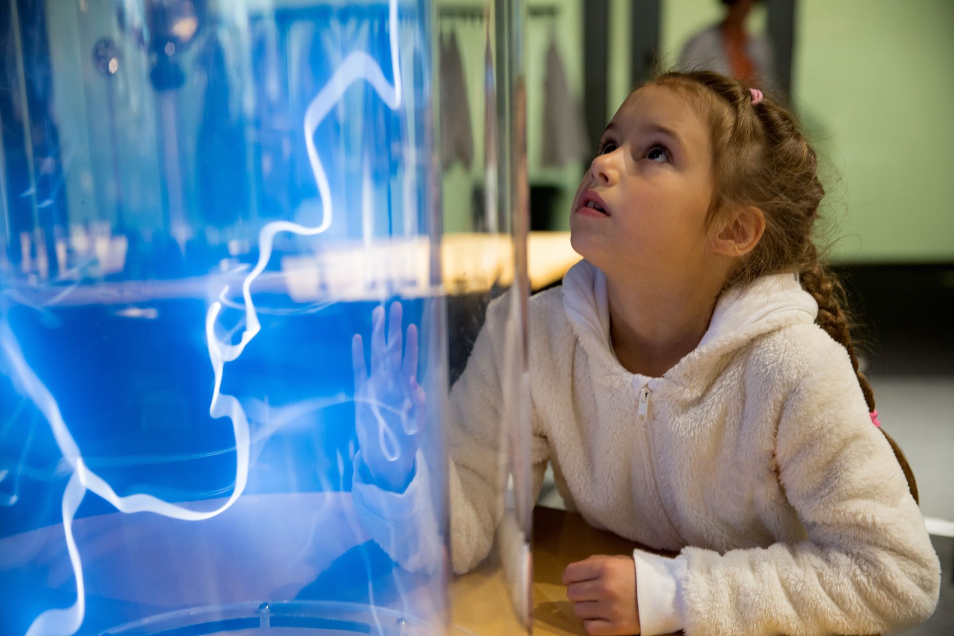 A little girl is looking at a lightning display in a museum.