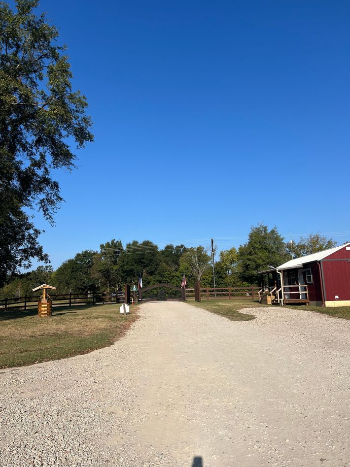 A gravel road leading to a red barn on a sunny day