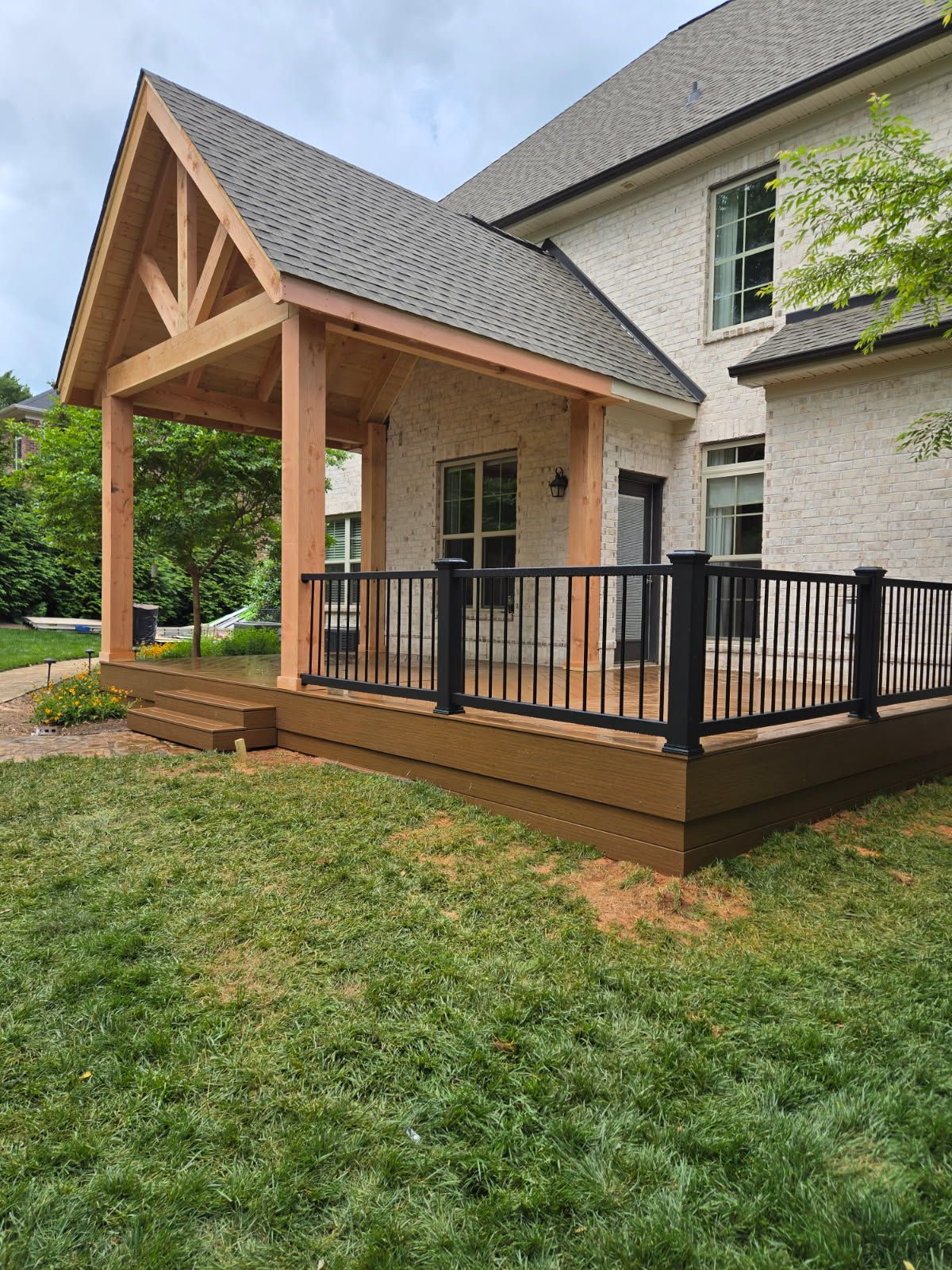 A wooden deck with a covered porch attached to a brick house, set in a grassy yard.