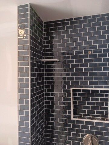 Dark blue subway tile shower, white niche and shelf, corner of room.