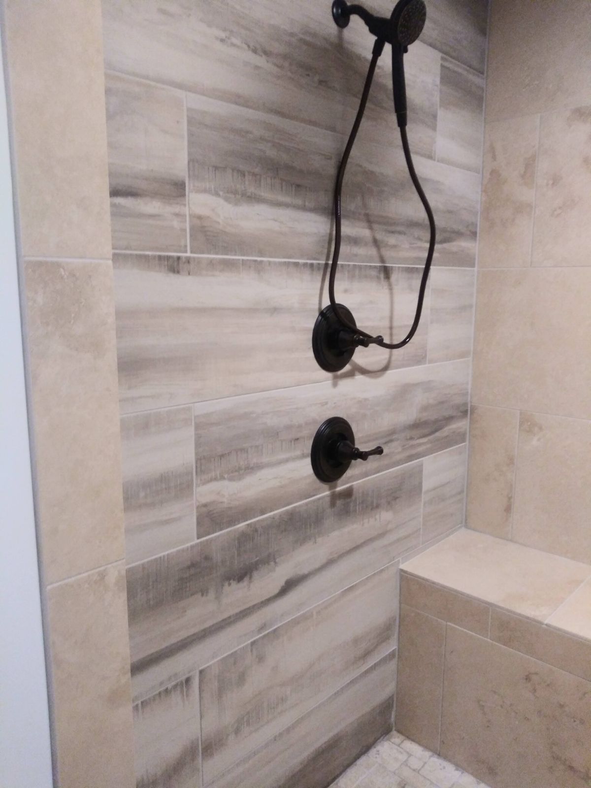 Shower with gray and beige wood-look tiles, dark fixtures, and a built-in bench.