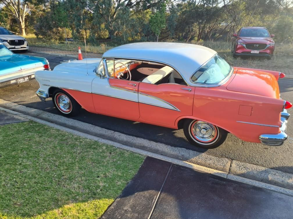 A pink and white car is parked on the side of the road.