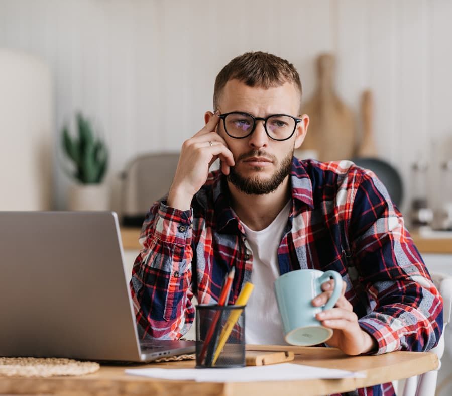 A man is sitting at a table with a laptop and a cup of coffee.