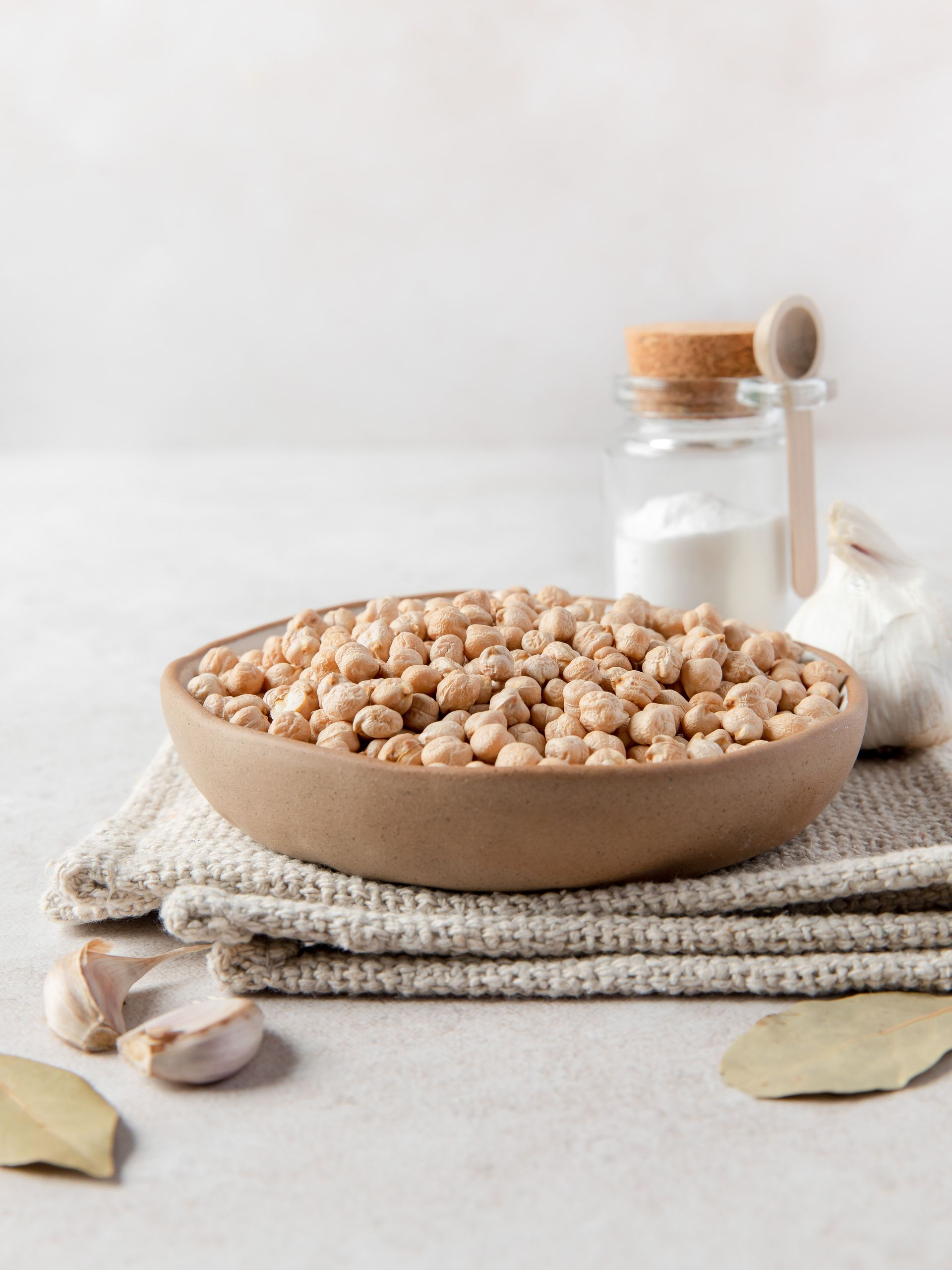 a bowl of chickpeas is sitting on a towel next to garlic and salt .