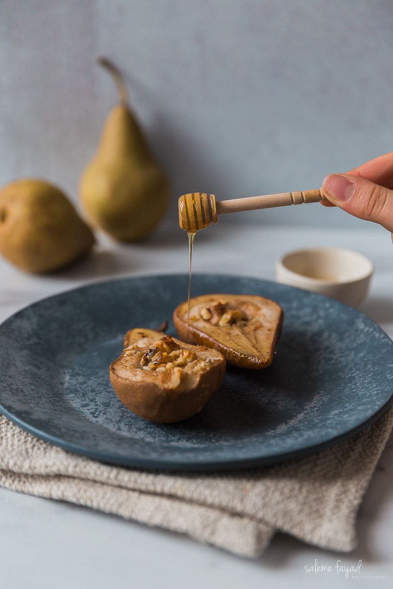 a person is pouring honey on a pear on a blue plate .