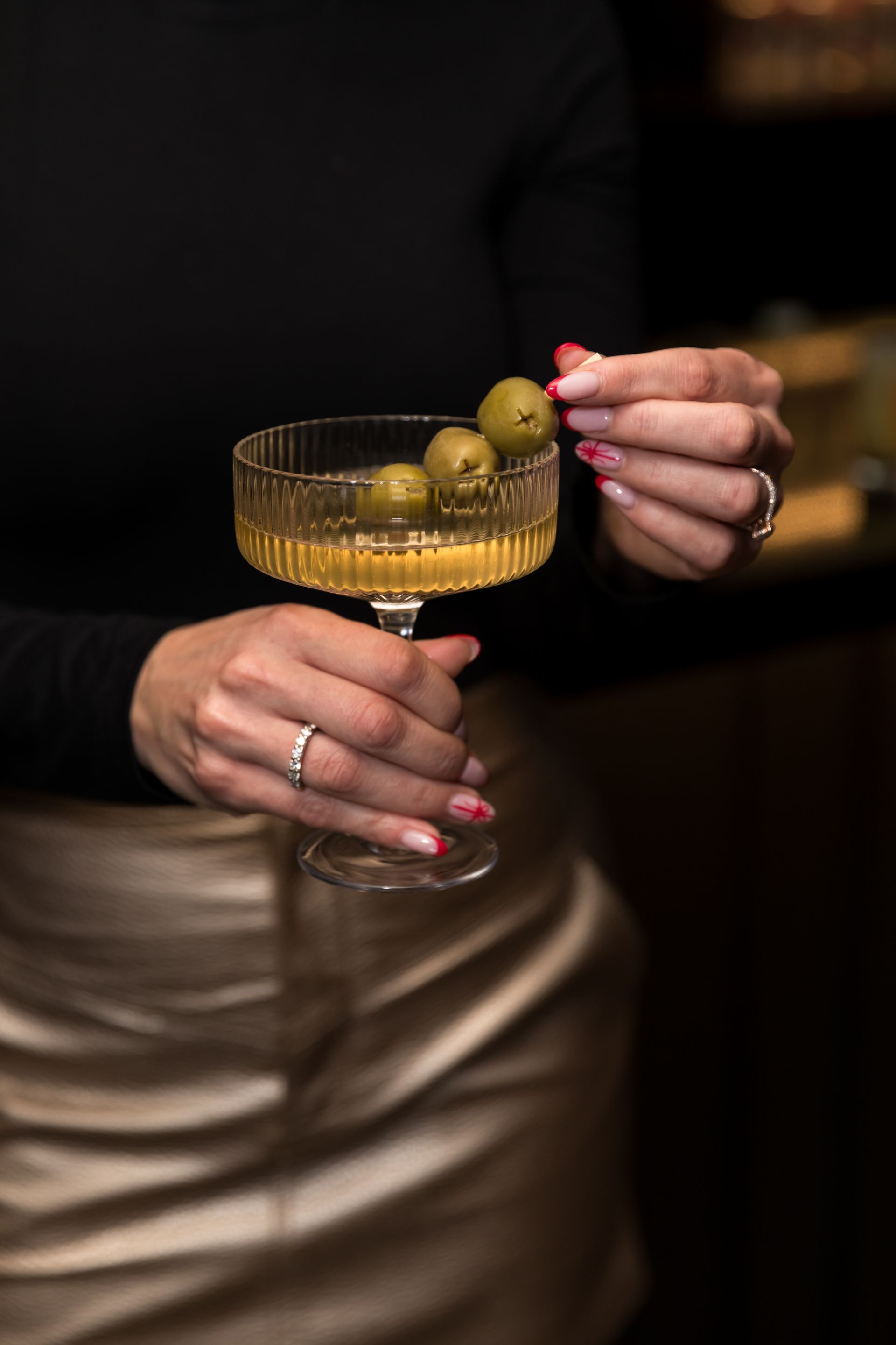 a woman is holding a martini glass with olives in it .