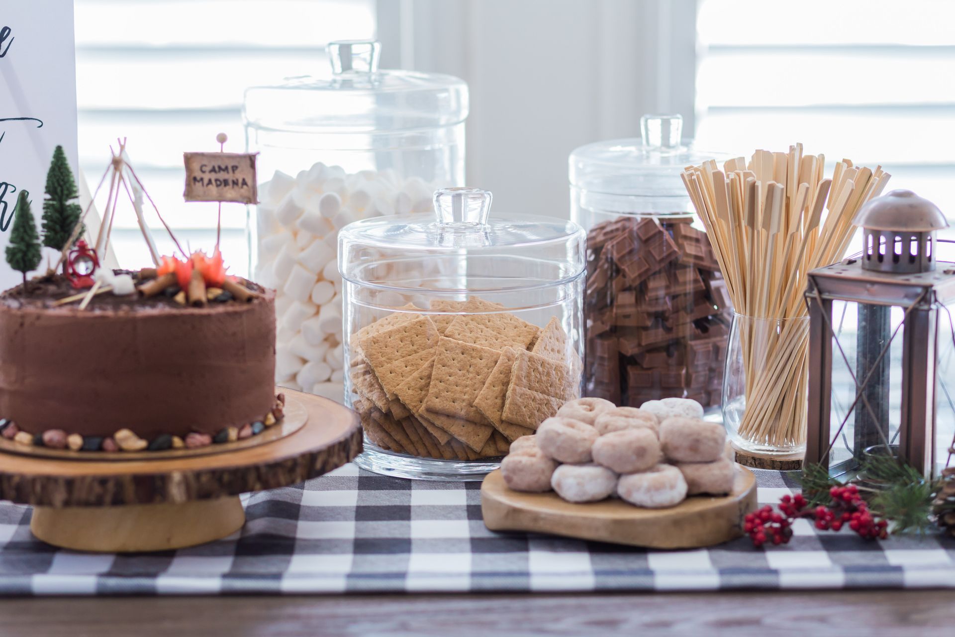 a table topped with a cake, s'mores , and other camp themed desserts.