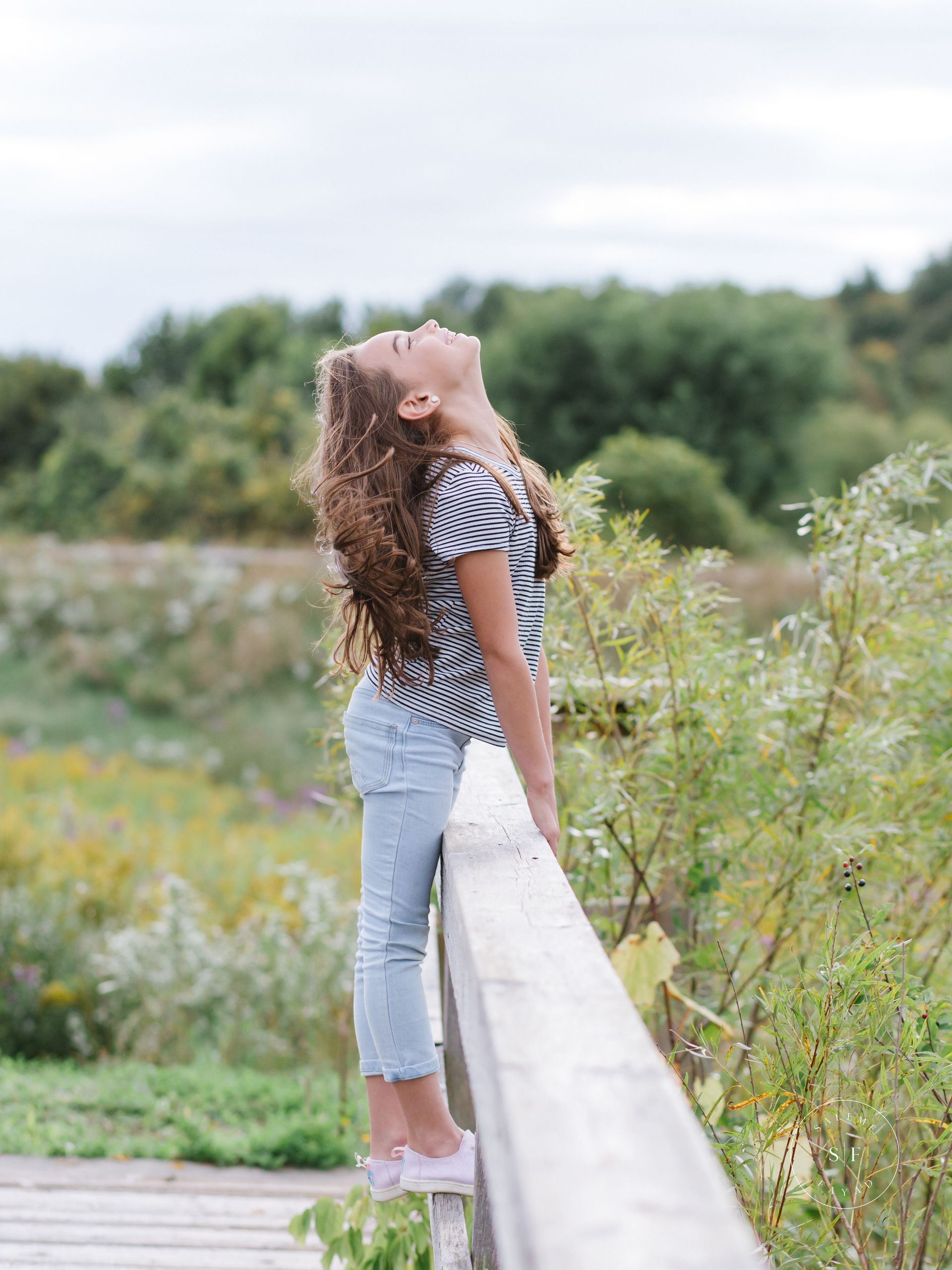 a little girl is standing on a wooden railing looking up at the sky .