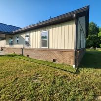 Side view of a tan house with a brick base and brown trim, set in a grassy yard under a blue sky. Side view of a tan house with a brick base and brown trim, set in a grassy yard under a blue sky.