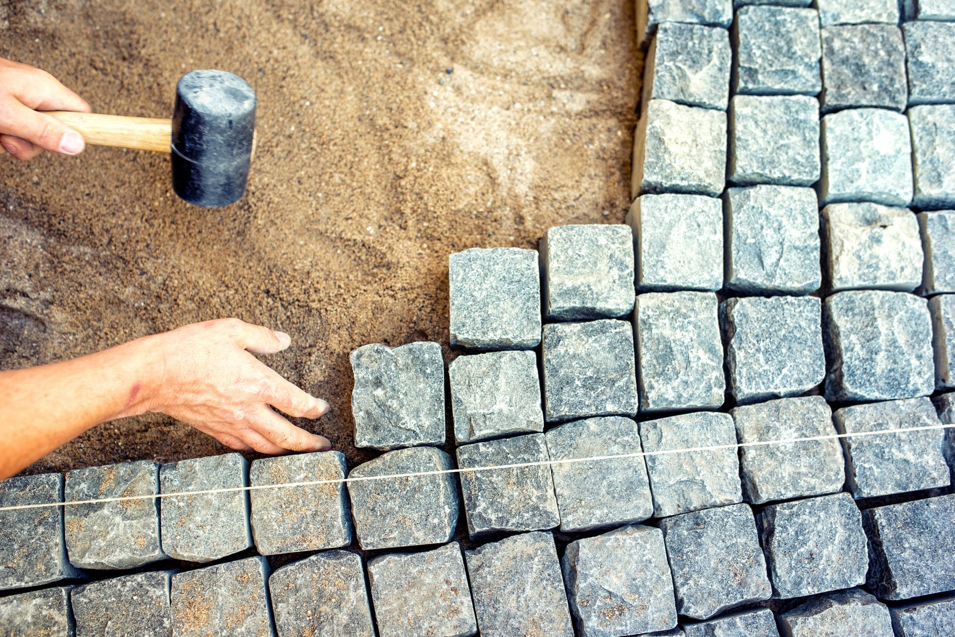 Person laying cobblestone pavers with a mallet, set in sand. Person laying cobblestone pavers with a mallet, set in sand.