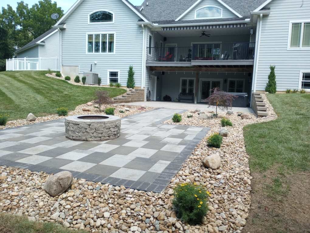 Backyard patio with checkerboard pavers, fire pit, and landscaping next to a multi-story house.