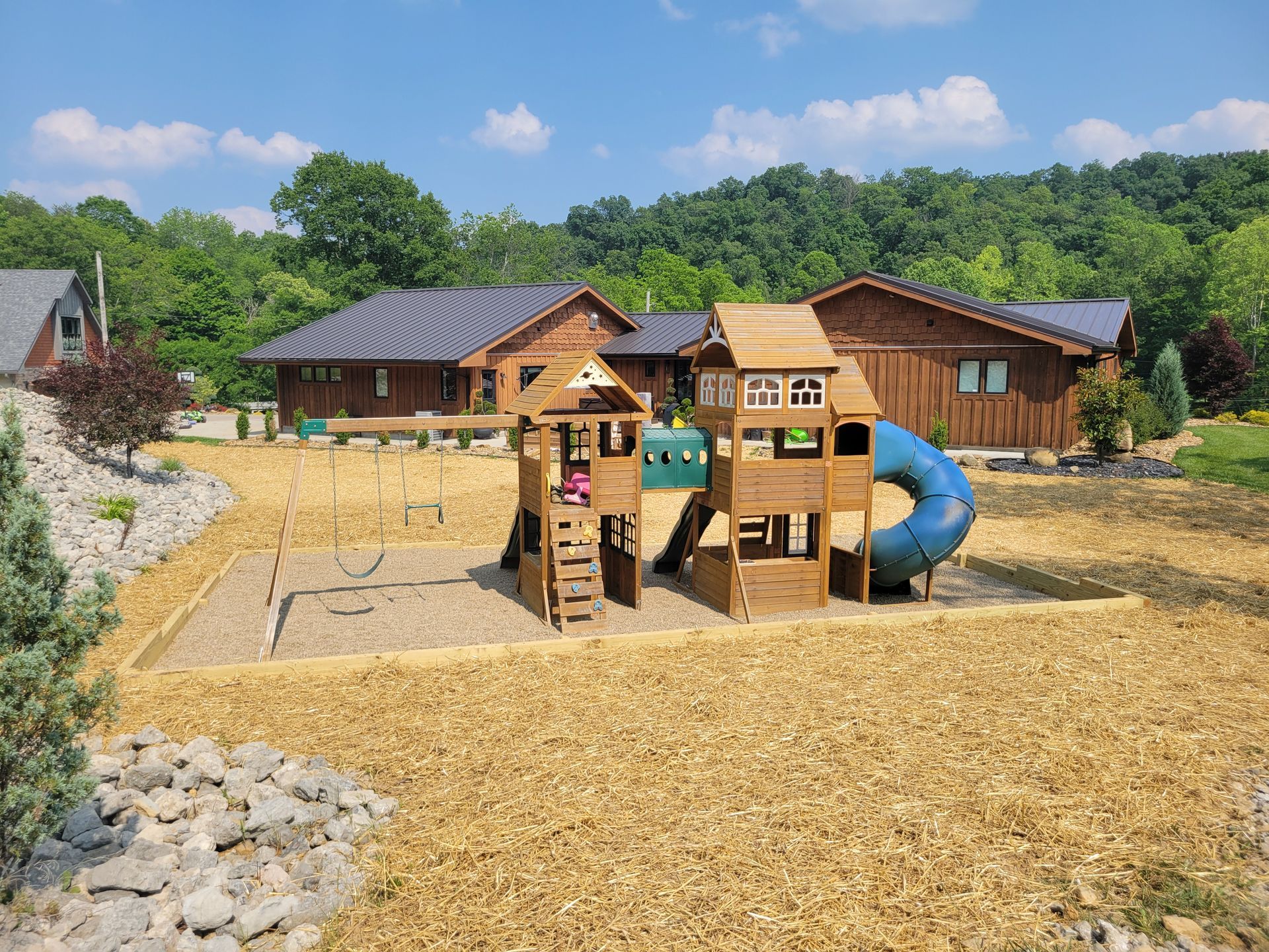 Playground with wood structures, blue slide, wood chips, and buildings in the background.