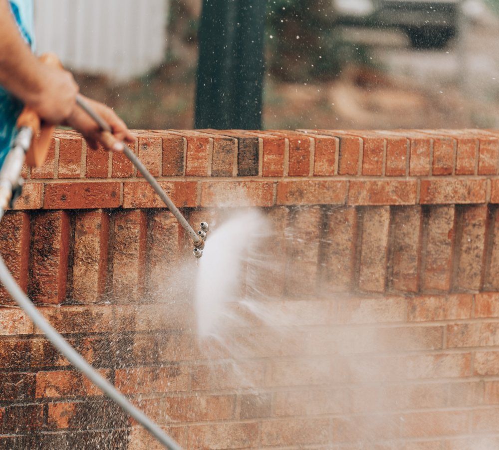 A Person Is Cleaning A Brick Wall With A High Pressure Washer — Out On A Limb Tree and Garden Care In Broulee, NSW