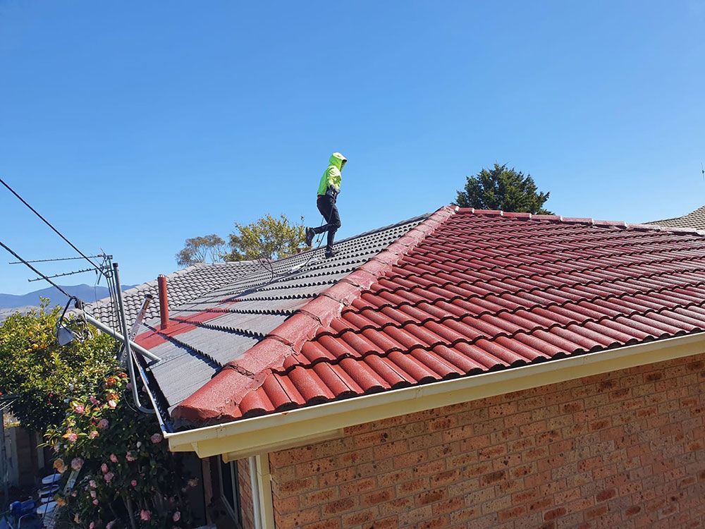 A Man Is Painting A Red Tiled Roof — ACT Roofing in Ngunnawal, ACT
