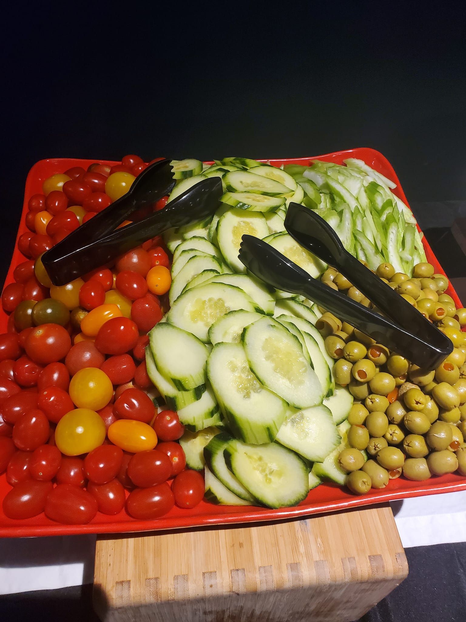 a tray of sliced cucumbers tomatoes and olives with tongs