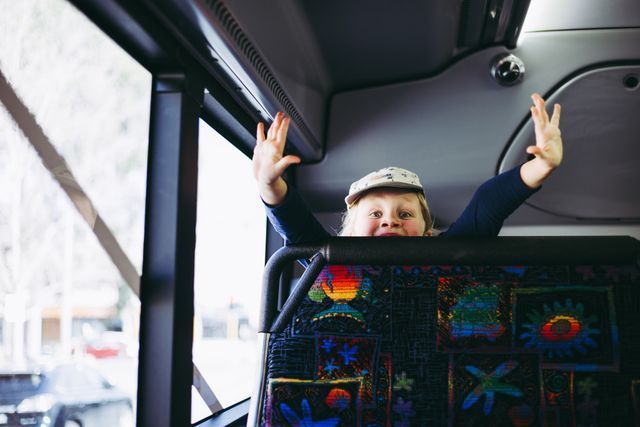 Child With Raised Arms Sits on a Bus Seat — J & B Bus and Coach Pty Ltd In Tweed Heads, NSW