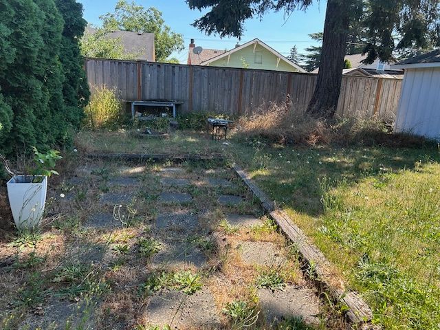 A backyard with a wooden fence and a concrete walkway.