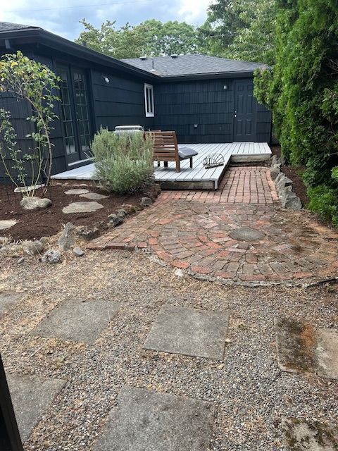 There is a brick walkway leading to a deck in the backyard of a house.