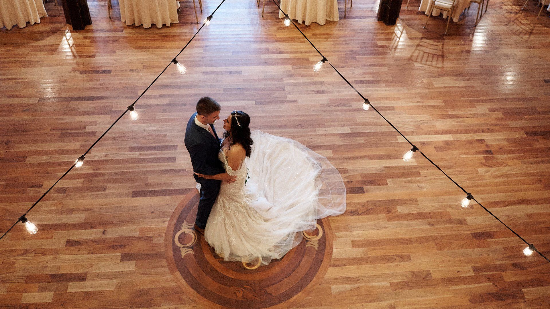 A bride and groom are dancing on a wooden floor at their wedding reception.