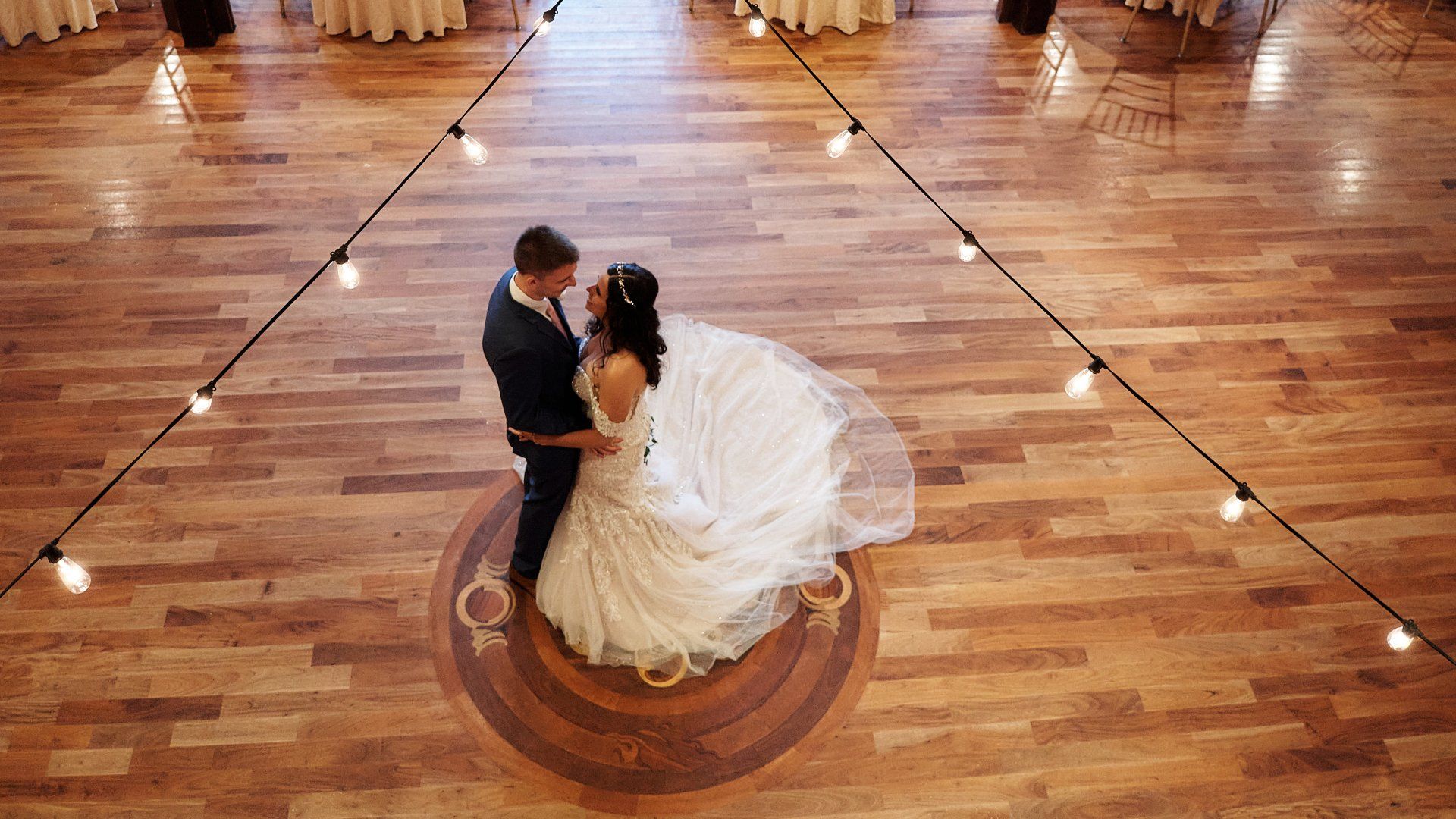 A bride and groom are dancing on a wooden floor at their wedding reception.