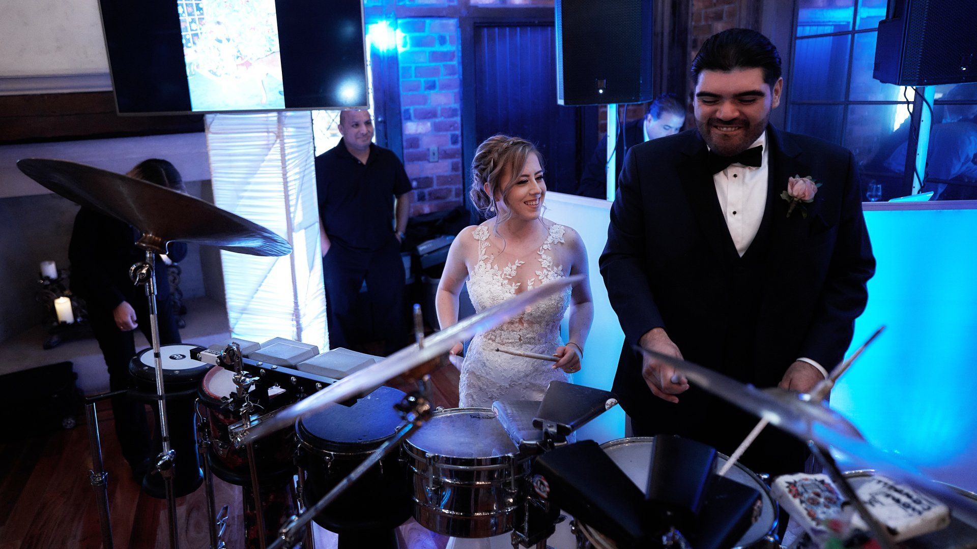 A bride and groom are playing drums at their wedding reception.