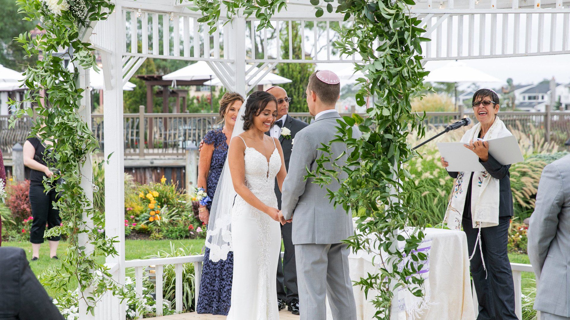 A bride and groom are holding hands during their wedding ceremony under a gazebo.