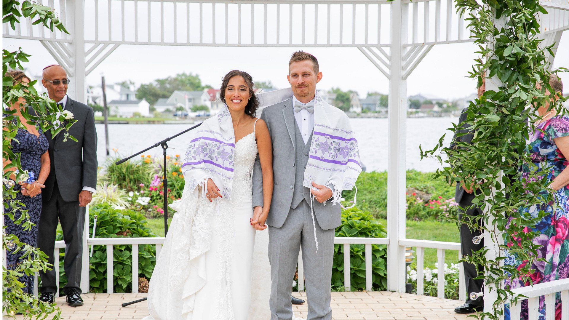 A bride and groom are standing under a gazebo holding hands.