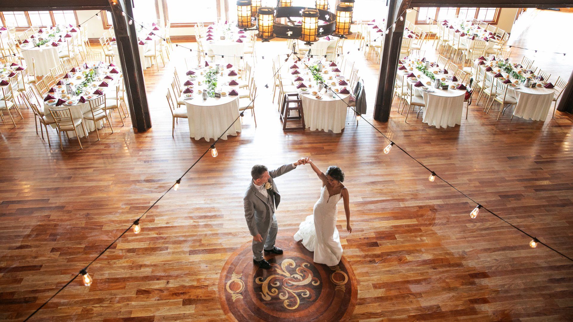 A bride and groom are dancing on a wooden floor in a large room.