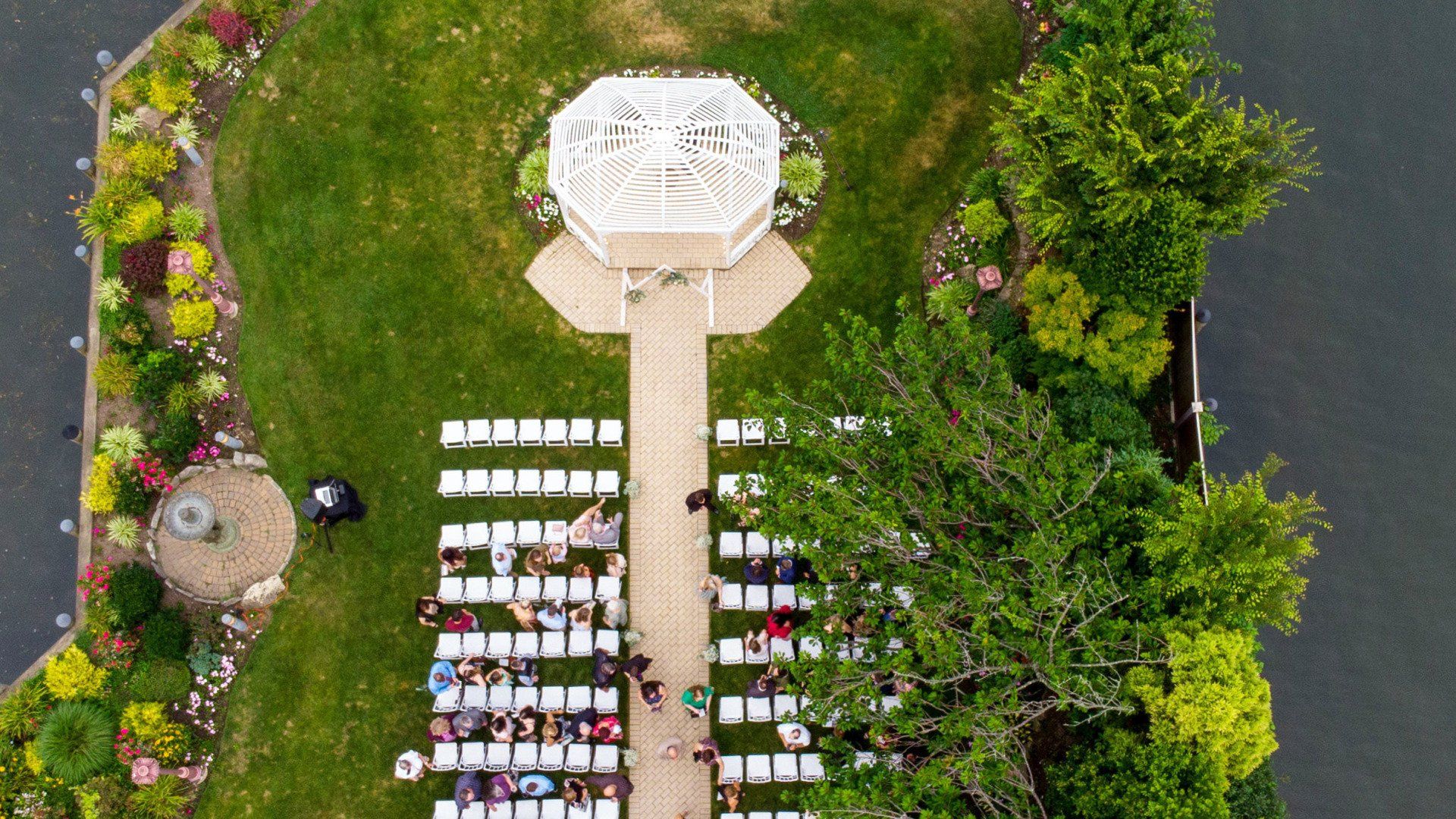 An aerial view of a wedding ceremony in a park with a gazebo.