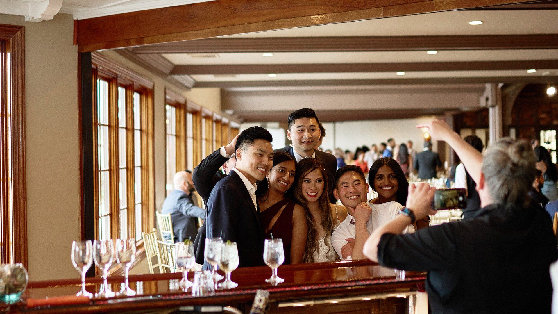 A group of people are posing for a picture in a room with wine glasses.