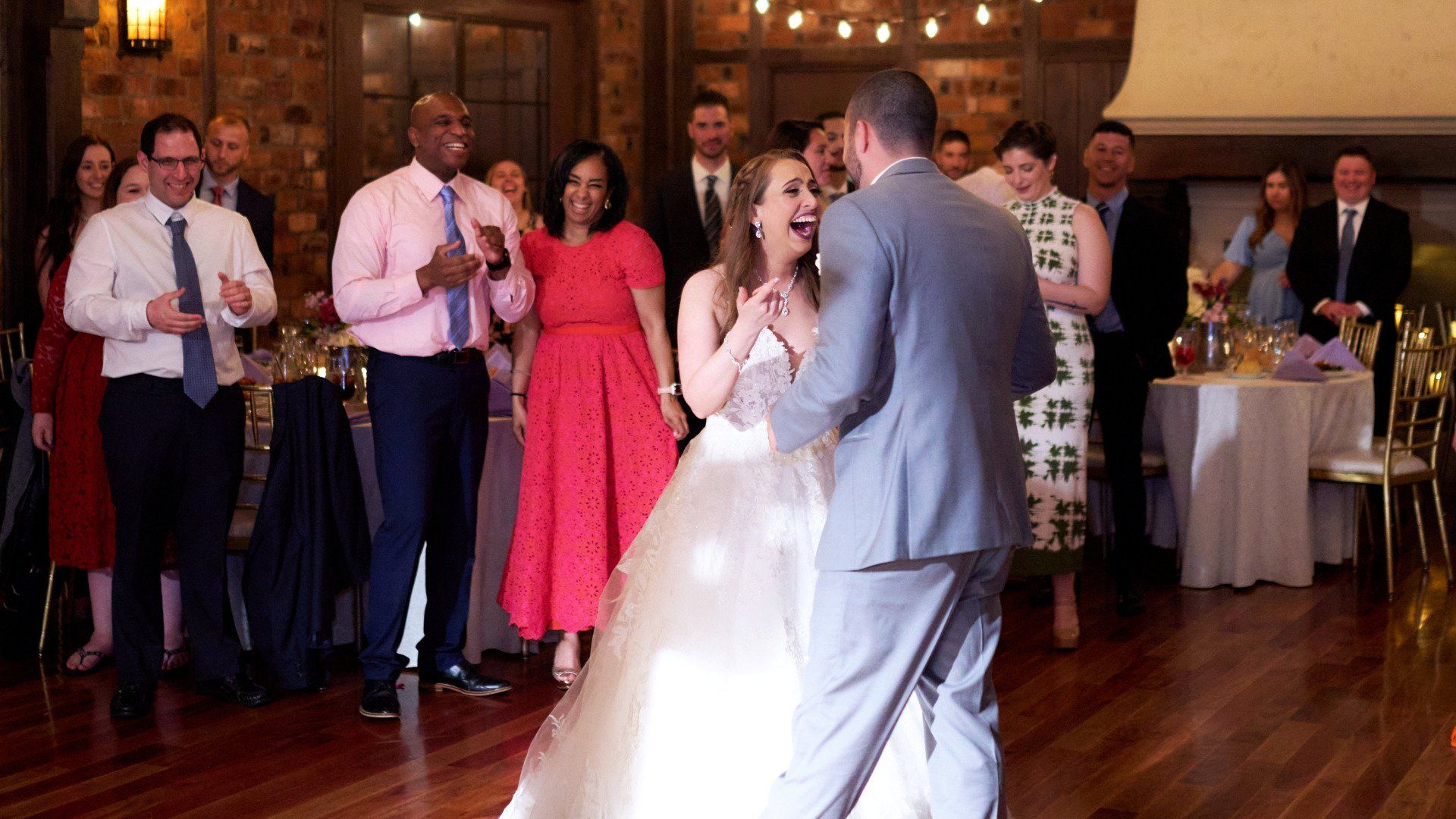 A bride and groom are dancing at their wedding reception in front of their wedding guests.
