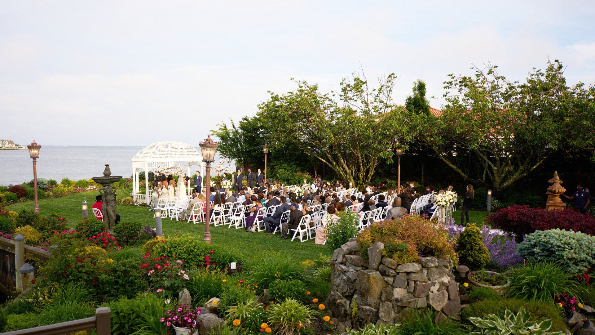 A wedding ceremony is taking place in a garden next to the ocean.